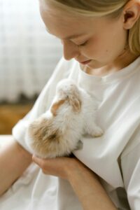 A young woman gently holds a fluffy bunny indoors, showcasing a tender human-animal connection.